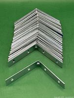 Stacked zinc plated metal corner braces arranged in a neat pile, showing the uniformity and size of the braces