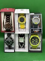 All six watches in their boxes displayed against green background