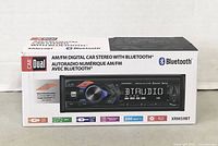 Photo of original packaging box of Dual XRM59BT AM/FM digital car stereo with Bluetooth, showing product image and key features.