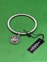 Silver-tone bracelet with purple and yellow enamel charm and Nomada brand tag