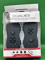 Front view of the Nyko Dualies motion controller set in original packaging, showing two black controllers and the front of a damaged box.