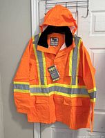Front view of a bright orange Viking Safety Maxx 150 waterproof rain jacket with reflective stripes and hood, on a hanger.