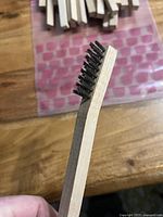 Close-up of a single wire brush showing wooden handle and black metal bristles