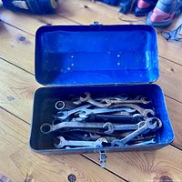 Blue metal toolbox open showing various wrenches inside on a wooden floor.