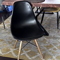 Front view of the black plastic chair with wooden legs placed on a patterned rug beside a wooden dining table.