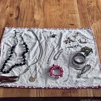 Full layout of costume jewelry assortment displayed on white cloth showing necklaces, bracelets, earrings, bangles, and cuff links on wooden surface.