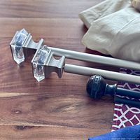 Close-up of two curtain rods showing one with clear rectangular acrylic finials and another with dark brown round finials.
