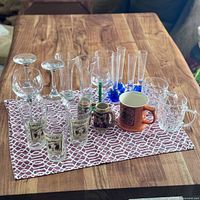 Random assortment of drinking glasses and mugs on a patterned cloth on wooden table
