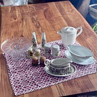 Overview photo of the lot showing all items on a tablecloth: 2 gravy boats, 4 sets of salt and pepper shakers, glass cake stand.
