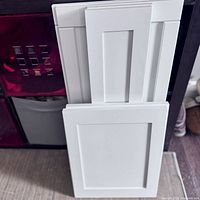 Six grey painted MDF cabinet doors leaning against a wall with visible clean edges and recessed panel design.
