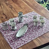 Photo showing hot chocolate pot, four espresso cups, and Limoges dish arranged on purple patterned cloth.