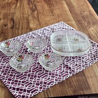 Four diamond cut Lubiana glass dessert bowls with floral designs and a frosted divided serving dish on a patterned placemat on a wooden table.