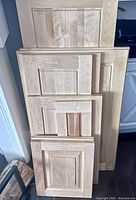 Front view of 10 different sized maple cabinet doors stacked for display, showing wood grain and panel details