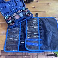 Photo showing the sanding drum set and sanding sleeves in the plastic storage case with the reciprocating saw blades rolled out beside it on a wooden surface.