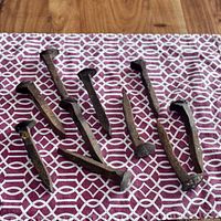 Photo showing 10 weathered metal railway spikes laid out on patterned fabric, highlighting their size, shape, and rustic condition.