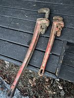 Two Ridgid pipe wrenches, one 36 inch and one 24 inch, showing heavy use with worn paint and rust on a black wooden surface.