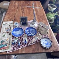 Full overview of lot items on wood table showing mix of ceramics, figurines, wall hangings and decor pieces