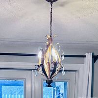 Photo of vintage candleabra chandelier hanging from ceiling, showing four light bulbs on curved arms with decorative glass drops