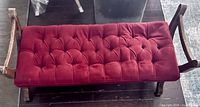 Top-down view of vintage wooden bench with red tufted upholstery cushion showing wear and wooden frame.