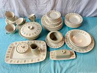 Full lot overview arranged on blue cloth showing multiple plates stacked, cups, and lidded serving dishes with olive branch motif