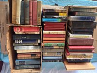 Wide view of three boxes containing hardcover books of various sizes and conditions, arranged vertically and stacked.