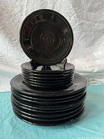 Stack of black Fiesta plates with one plate displayed upright showing the classic concentric ring design and glossy black glaze with some wear.