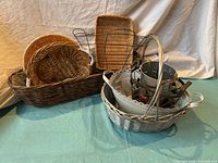 Photo showing assorted natural and white woven baskets, some oval and round, stacked together with metal hangers inside a white basket.