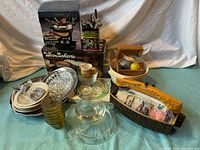 Overview of the mixed kitchen lot showing all items including Pyrex dishes, dough bowls, iced tea spoons, hammered aluminum tray, and other accessories on a blue cloth.