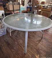 View of round outdoor table with heavy glass top and powder-coated metal frame, showing the umbrella hole and four supporting legs.