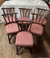 Set of six mid-century rattan chairs grouped together with pink cushioned seats in front of a covered background.