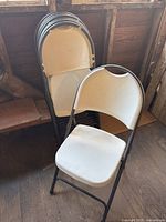 Eight stacked folding chairs showing beige seats and black metal frames.