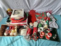 Mixed lot of vintage holiday items displayed including Spode Christmas Tree plate, Snowman cake pan, Christmas ornaments, candles, and assorted seasonal fabric pieces.