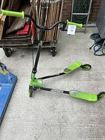 Front-left angled side view of the three-wheel Sporter scooter showing the black frame with green foot platforms and green handle grips.