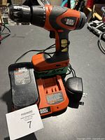 Black & Decker cordless drill standing on charging dock with battery attached, charger visible.