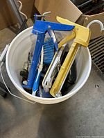 Top view of 5 gallon bucket showing two staple guns, a blue brush, and other metallic hand tools inside the bucket.
