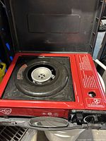 Red Max brand single burner portable camp stove with a red metal body and black burner area. Control knob on side.