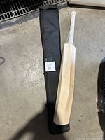 Cricket bat laying next to the black soft carrying case on concrete floor.