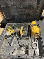 Open black molded plastic case containing the yellow and black DeWalt cordless impact driver, battery, and charger with dust inside case