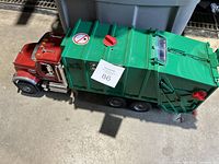 Top view of toy garbage truck showing red cab and green container body with label and red knobs on top.
