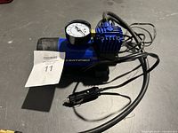 Mini air compressor showing pressure gauge, blue body, black cables, and cigarette lighter plug for power.