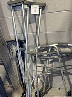 Pair of aluminum crutches, one folding walker, and two canes leaning against a wall
