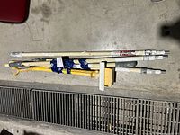 Full view of five painting poles and a yellow pole holder laid on concrete floor showing paint residue and dirt.