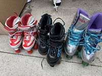 Three pairs of roller skates: white/red adjustable kids skates, black inline skates, silver and purple Impala quad skates.