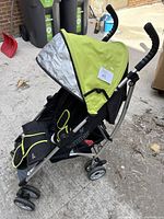 Side view of black stroller with lime green canopy and accents, folded for transport or standing open outdoors
