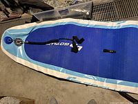 Top view of the inflatable stand up paddle board showing the blue textured surface and white edging with ankle leash attached.