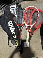 Four tennis rackets including Wilson branded covers; three rackets appear with covers and one without. Various colors and grip conditions.