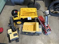 Four used toy trucks grouped on floor including two dump trucks, a forklift, and a crane truck.