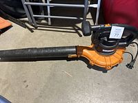 Electric leaf blower laid on ground showing full length including blower tube and power cord.