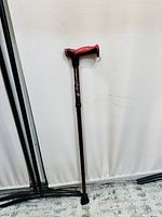 Full view of the foldable walking stick with red and black ergonomic handle, maroon shaft, and rubber sole tip.