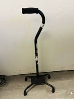 Front view of the black quad cane with foam grip and four wide rubber tips for stability.